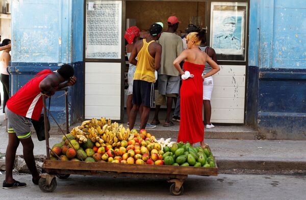 رجل يمسك بعربة مليئة بالفاكهة أمام متجر، كما تُرى صورة للرئيس الكوبي السابق راؤول كاسترو على جداره في هافانا، كوبا  21 تموز / يوليو 2018 - سبوتنيك عربي