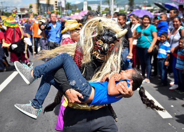 رجل يرتدي قناعا لمخلوق أسطوري، يحمل فتاة بين ذراعيه خلال عرض في سان سلفادور، 1 أغسطس/ آب 2018 - سبوتنيك عربي