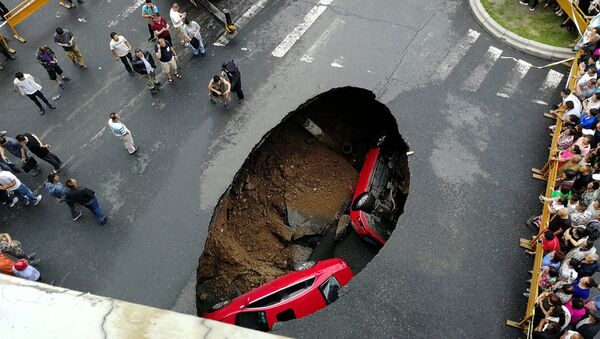 أشخاص يتجمعون حول حفرة سقطت فيها سياراتان وسط شارع في مدينة هاربين، الصين 4 أغسطس/ آب 2018 - سبوتنيك عربي