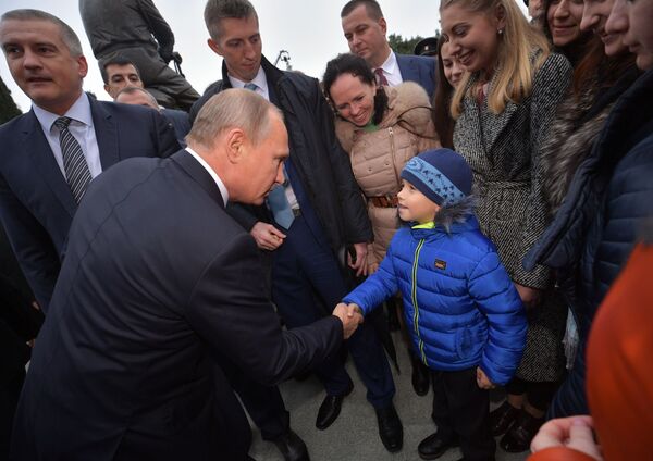 الرئيس فلاديمير بوتين يصافح طفلا أثناء لقائه مع المواطنين، بعد مراسم افتتاح نصب تذكاري للإمبراطور ألسكندر الثالث في يالطا، 18 نوفمبر/ تشرين الثاني 2018 - سبوتنيك عربي