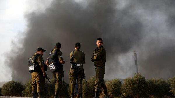 جنود إسرائيليون بالقرب من السياج الحدودي على الجانب الإسرائيلي من الحدود مع قطاع غزة واحتجاج فلسطينيين على الجانب الآخر - سبوتنيك عربي