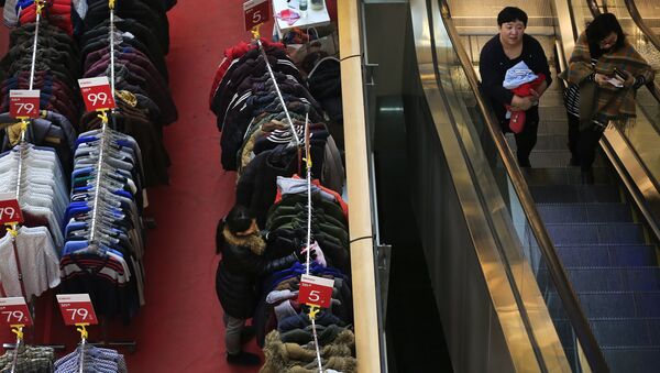 Women take an escalator near a salesperson wipes the winter clothes during a promotion sale at a shopping mall in Beijing, Wednesday, Jan. 13, 2016 - سبوتنيك عربي