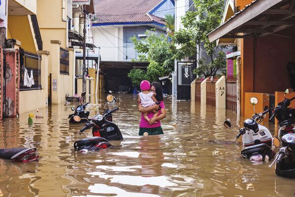 امرأة تحمل طفلها وسط مياه غمرت شوارع حي ماكاسار، إثر هطول أمطار غزيرة في إندونيسيا، 23 يناير/ كانون الثاني 2019 - سبوتنيك عربي