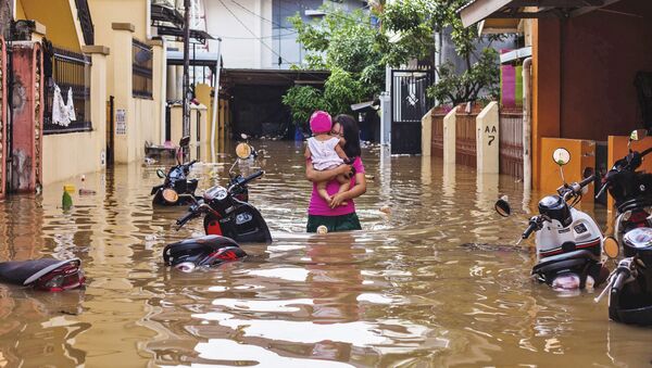 امرأة تحمل طفلها وسط مياه غمرت شوارع حي ماكاسار، إثر هطول أمطار غزيرة في إندونيسيا، 23 يناير/ كانون الثاني 2019 - سبوتنيك عربي