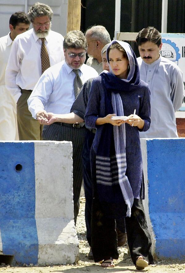 سفيرة النوايا الحسنة للمفوضية السامية للأمم المتحدة لشؤون اللاجئين، أنجولينا جولي، تسير مع مسؤولين في مركز كاشا غاري لإعادة اللاجئين إلى وطنهم خارج بيشاور، في 5 مايو/ أيار 2005. - سبوتنيك عربي