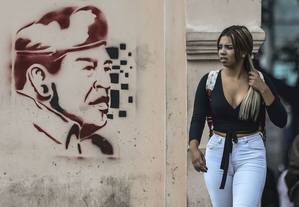 امرأة تسير على خلفية رسم غرافيتي لوجه الرئيس الفنزويلي السابق الراحل أوغو تشافيس في كاراكاس، فنزويلا 6 فبراير/ شباط 2019 - سبوتنيك عربي