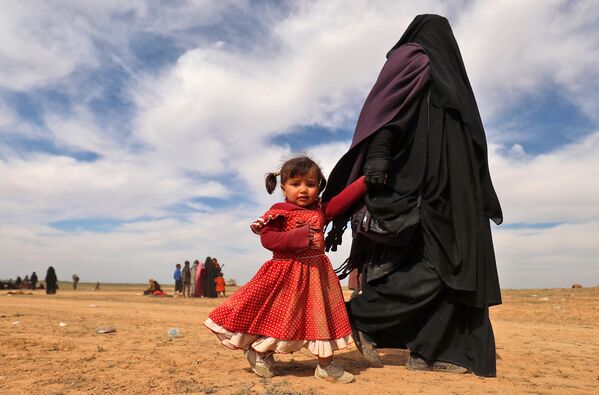 امرأة منقبة، لاجئة، تسير مع طفلتها يخلون منطقة باغوز، خلال عملية قامت بها القوات الديمقراطية السورية المدعومة من الولايات المتحدة لطرد تنظيم داعش الإرهابي من المنطقة، في محافظة دير الزور السورية الشرقية، سوريا 13 فبراير/ شباط 2019 - سبوتنيك عربي