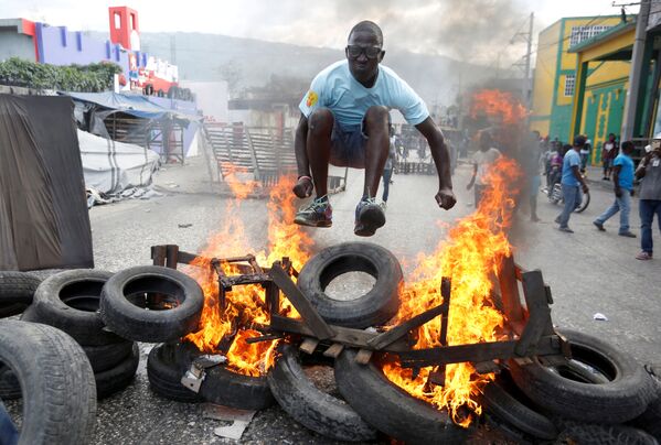 متظاهر يقفز فوق حاجز محترق أثناء احتجاجات ضد الحكومة في شوارع بورت أو برنس، هايتي، 10 فبراير/ شباط 2019 - سبوتنيك عربي