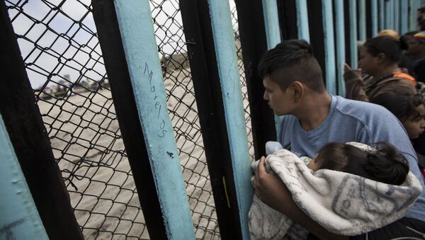 مهاجر يحمل ولده على الحدود بين المكسيك وأمريكا - سبوتنيك عربي