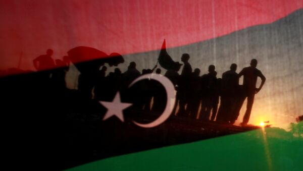 ليبيون يظهرون من خلال علم مملكة ليبيا خلال مسيرة الاحتفال أمام مقر القذافي في مجمع باب العزيزية في طرابلس - سبوتنيك عربي
