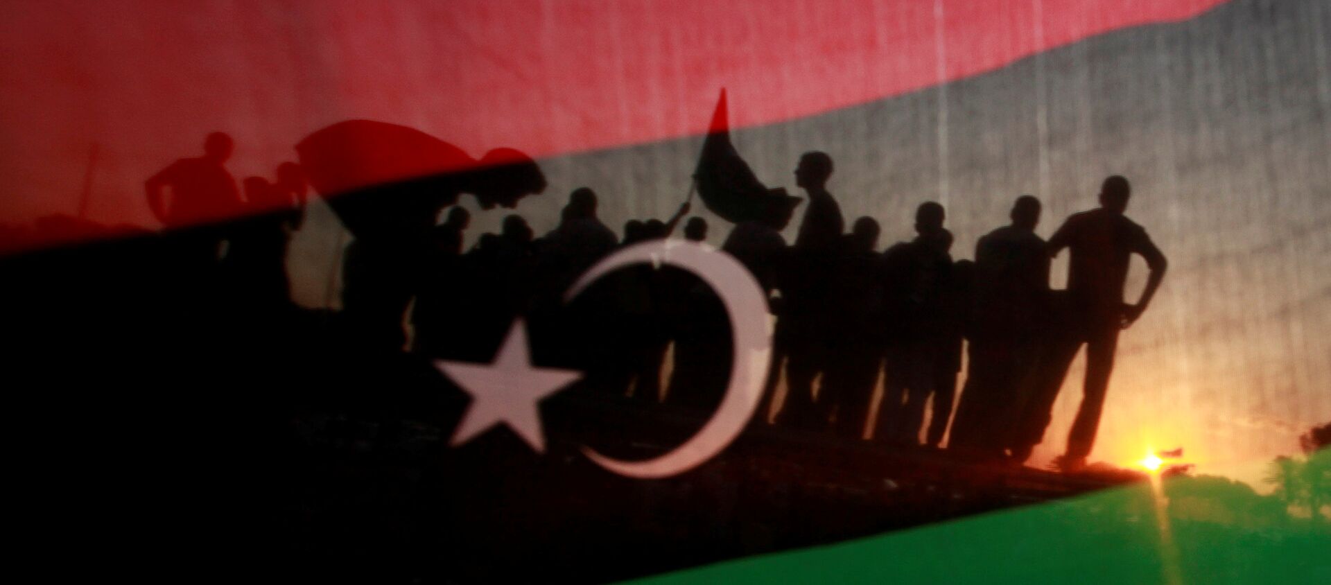 ليبيون يظهرون من خلال علم مملكة ليبيا خلال مسيرة الاحتفال أمام مقر القذافي في مجمع باب العزيزية في طرابلس - سبوتنيك عربي, 1920, 02.02.2021