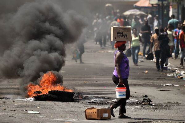 امرأة تسير على خلفية تظاهرات في أحد شوارع بورت-أو-برينس، هاييتي 17 فبراير/ شباط 2019 قدمت الحكومة مجموعة من الاجراءات الاقتصادية لمحاولة تهدئة الأزمة السياسية. من بينها، أعلنت الحكومة هدفها المتمثل في خفض سعر الأرز بنسبة 30% - سبوتنيك عربي