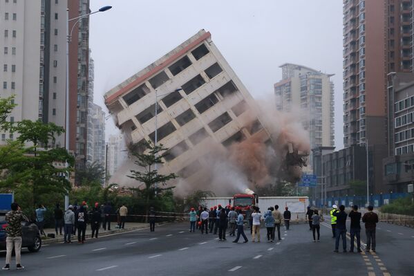 مواطنون يراقبون عملية هدم مبنى مكون من ثمانية طوابق يقع على طريق في هايكو بمقاطعة هاينان، الصين في 24 فبراير/ شباط 2019 - سبوتنيك عربي