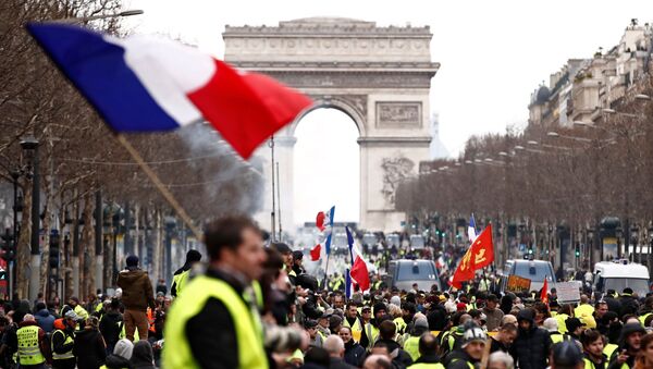 أحد المتظاهرين يرتدي سترة صفراء يلوح بعلم فرنسي وهو يقف على الشانزليزيه بالقرب من قوس النصر أثناء مظاهرة حركة السترات الصفراء في باريس - سبوتنيك عربي