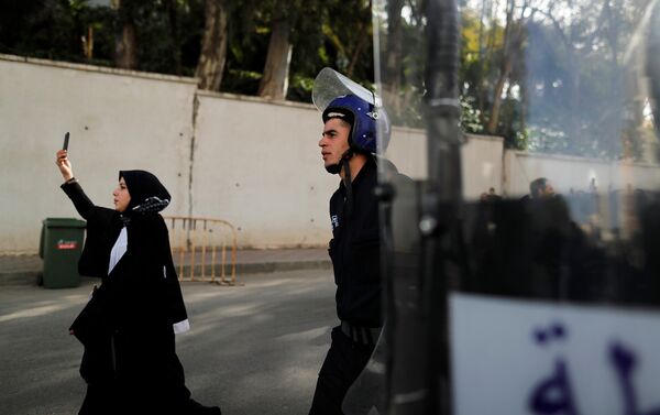 محامية تمسك هاتفها المحمول بالقرب من أحد أفراد الشرطة أثناء مسيرتها مع آخرين إلى المجلس الدستوري خلال احتجاج للاحتجا على ترشح بوتفليقة - سبوتنيك عربي