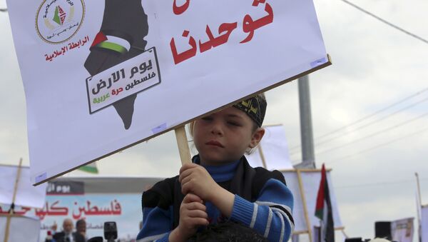 طفل فلسطيني يحمل لافتة الأرض توحدنا، فلسطين أرض عربية، خلال مسيرة بمناسبة يوم الأرض في بيت حانون، بالقرب من حدود القطاع مع إسرائيل 30 مارس/ آذار 2016 - سبوتنيك عربي
