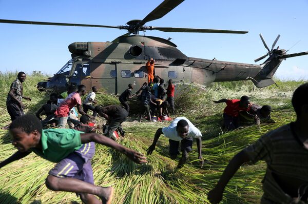 سكان محليون يركضون باتجاه طائرة هليكوبتر تابعة لجيش الدفاع الوطني لجنوب إفريقيا، التي نقلت المساعدات الغذائية إلى القرية المتضررة من الإعصار أيداي، موزمبيق 26 مارس/ آذار 2019 - سبوتنيك عربي