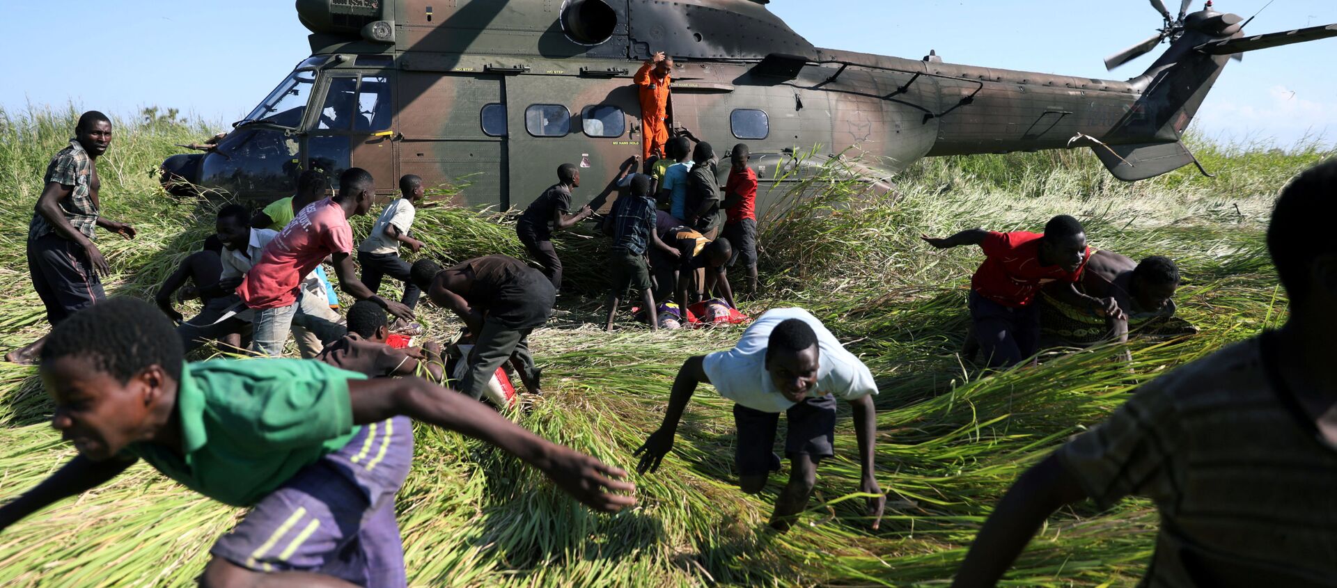 سكان محليون يركضون باتجاه طائرة هليكوبتر تابعة لجيش الدفاع الوطني لجنوب إفريقيا، التي نقلت المساعدات الغذائية إلى القرية المتضررة من الإعصار أيداي، موزمبيق 26 مارس/ آذار 2019 - سبوتنيك عربي, 1920, 02.04.2021