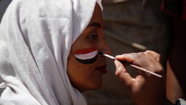 رجل يرسم العلم السوداني على وجه المتظاهرين في الخرطوم - سبوتنيك عربي