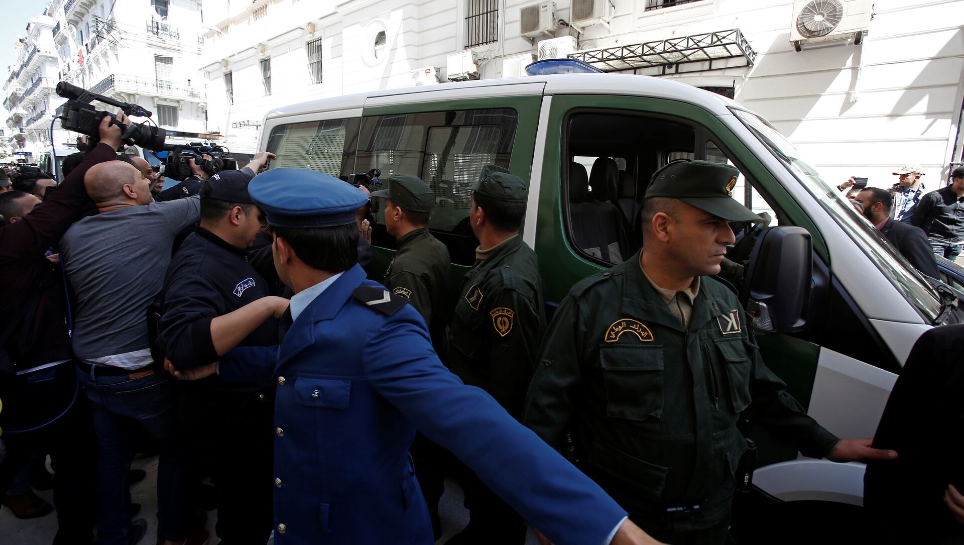 وسائل الإعلام والشرطة تحيط بقافلة من مركبات الشرطة بينما يتم نقل رجل أعمال مشتبه به إلى المحكمة في الجزائر - سبوتنيك عربي, 1920, 13.10.2021