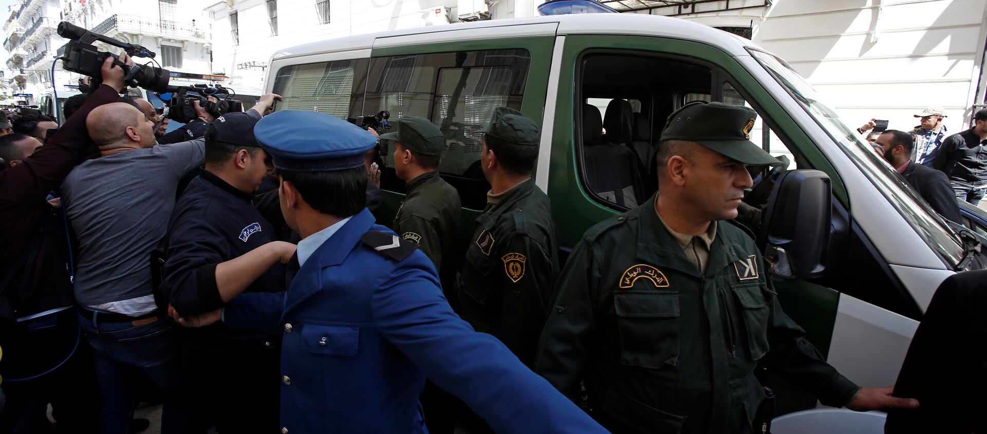 وسائل الإعلام والشرطة تحيط بقافلة من مركبات الشرطة بينما يتم نقل رجل أعمال مشتبه به إلى المحكمة في الجزائر - سبوتنيك عربي, 1920, 13.10.2021