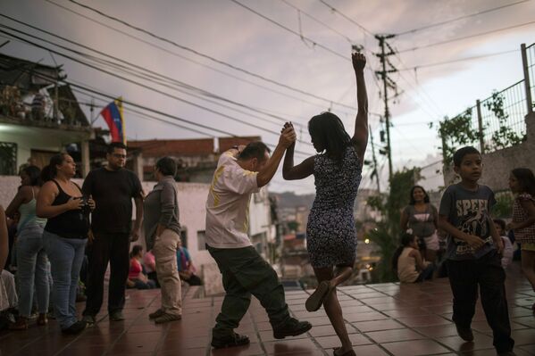 شخصان يرقصان على عزف موسيقيين في ساحة عامة حيث يجتمع الجيران في كاراكاس، فنزويلا، عند غروب الشمس السبت 11 مايو/ أيار 2019 - سبوتنيك عربي