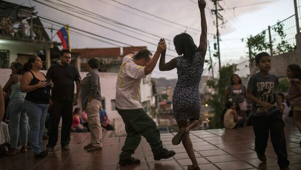 شخصان يرقصان على عزف موسيقيين في ساحة عامة حيث يجتمع الجيران في كاراكاس، فنزويلا، عند غروب الشمس السبت 11 مايو/ أيار 2019 - سبوتنيك عربي