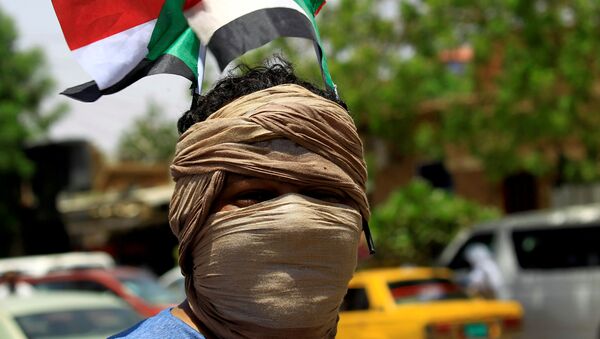 عضو في تحالف المعارضة والمجموعات الاحتجاجية في السودان يرتدي العلم الوطني وهو يهتف بشعارات خارج البنك المركزي السوداني - سبوتنيك عربي