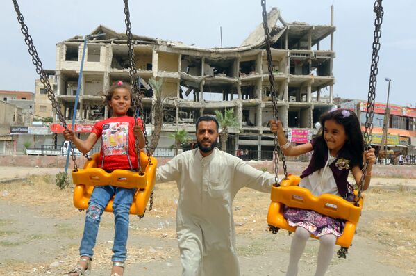 فتيات يركبن على أرجوحة بالقرب من مبنى مدمر في اليوم الأول من عيد الفطر في مدينة الرقة، سوريا 5 يونيو/ حزيران 2019 - سبوتنيك عربي
