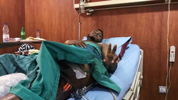 مصاب بعيار ناري في الحملة على المتظاهرين السودانيين يلوح بعلامة النصر داخل وهو يتلقى العلاج في مستشفى بالخرطوم - سبوتنيك عربي
