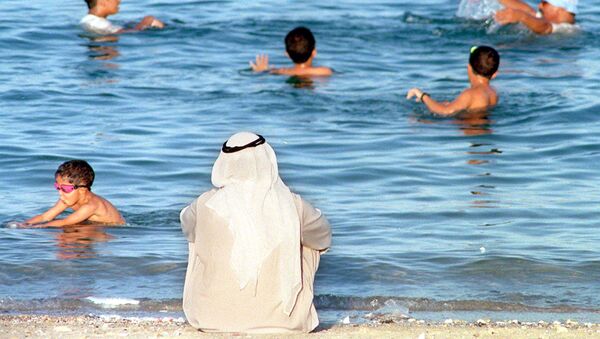 مواطن كويتي يراقب الأطفال وهم يسبحون في البحر بالكويت بالتزامن مع ارتفاع درجات الحرارة في البلاد - سبوتنيك عربي