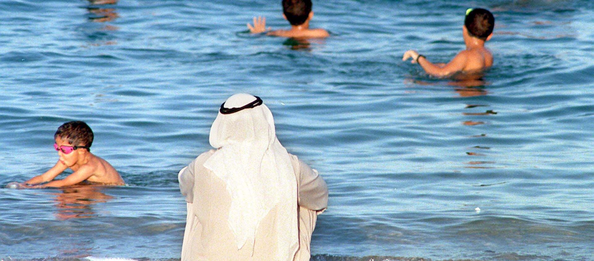 مواطن كويتي يراقب الأطفال وهم يسبحون في البحر بالكويت بالتزامن مع ارتفاع درجات الحرارة في البلاد - سبوتنيك عربي, 1920, 02.06.2021