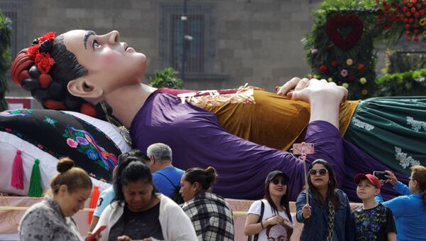 يلتقط الناس الصور بجوار تمثال كبير للفنانة المكسيكية فريدا كالو ملقاة على سرير خلال معرض لوس كولورز دي فريدا كالو في ميدان زوكالو في مكسيكو سيتي - سبوتنيك عربي