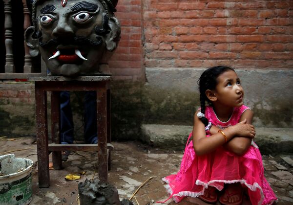 فتاة جالسة بجوار رأس تمثال شيطان غانتاكارن في مهرجان غنتاكارنا في نيبال، 30 يوليو/ تموز 2019 - سبوتنيك عربي