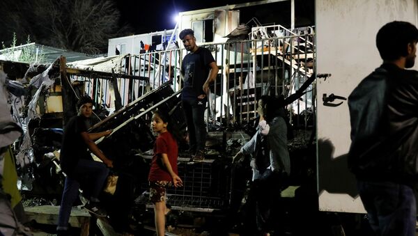 مهاجرون يقفون أمام حاويات محترقة في أعقاب نشوب حريق في مخيم موريا بجزيرة ليسبوس باليونان - سبوتنيك عربي