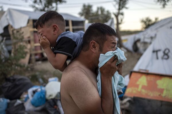 رجل مع طفل أثناء اشتباكات بالقرب من مخيم موريا للاجئين في جزيرة ليسبوس اليونانية، 29 سبتمبر 2019 - سبوتنيك عربي