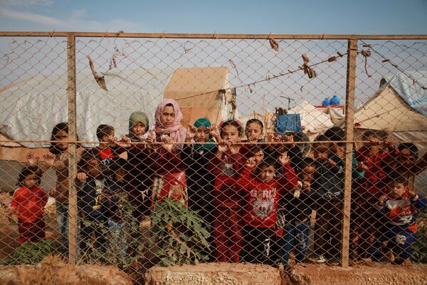 أطفال سوريون مهجرون يقفون خلف سياج مخيم كفر لوسين، في ريف إدلب الشمالي، الحدود السورية التركية، 22 أكتوبر 2019 - سبوتنيك عربي