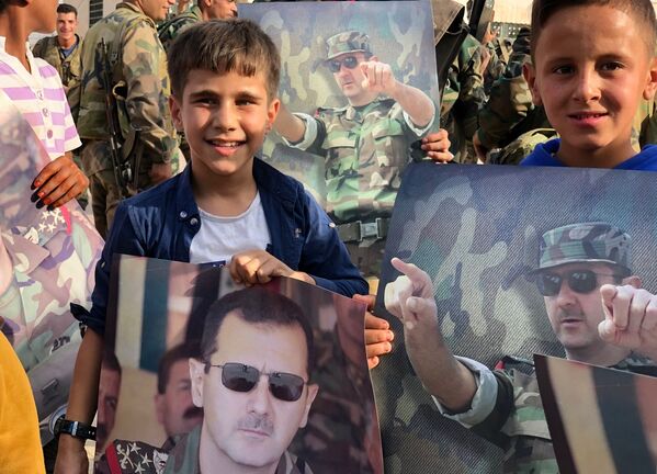 أطفال يحملون ملصقات عليها صورة للرئيس السوري بشار الأسد في مدينة منبج بعد دخول الجيش السوري إليها - سبوتنيك عربي