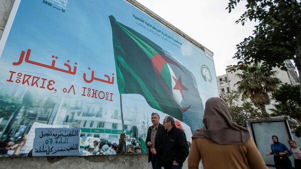 أشخاص يمشون بجوار ملصق حملة للانتخابات الرئاسية في الجزائر العاصمة - سبوتنيك عربي