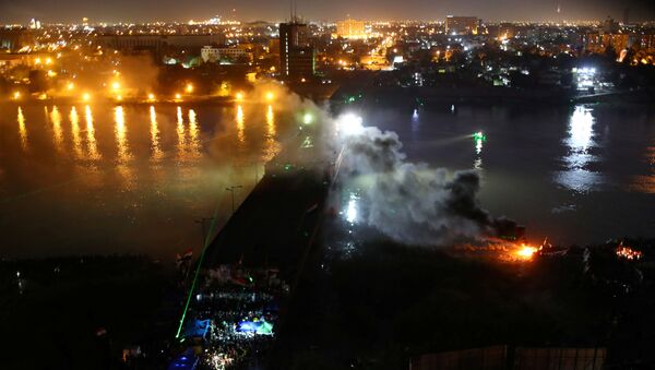 الدخان يتصاعد مع متظاهرين عراقيين يتشاجرون مع شرطة مكافحة الشغب خلال الاحتجاجات المناهضة للحكومة الجارية على جسر الجمهورية في بغداد - سبوتنيك عربي