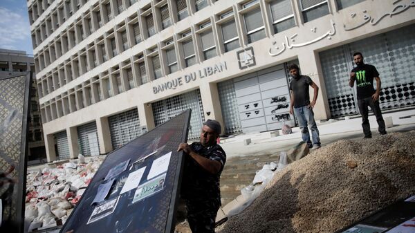 ضابط شرطة يرفع جزءًا من السياج بعد أن قام المتظاهرون بهدمه خارج البنك المركزي اللبناني خلال الاحتجاجات المستمرة المناهضة للحكومة في بيروت - سبوتنيك عربي