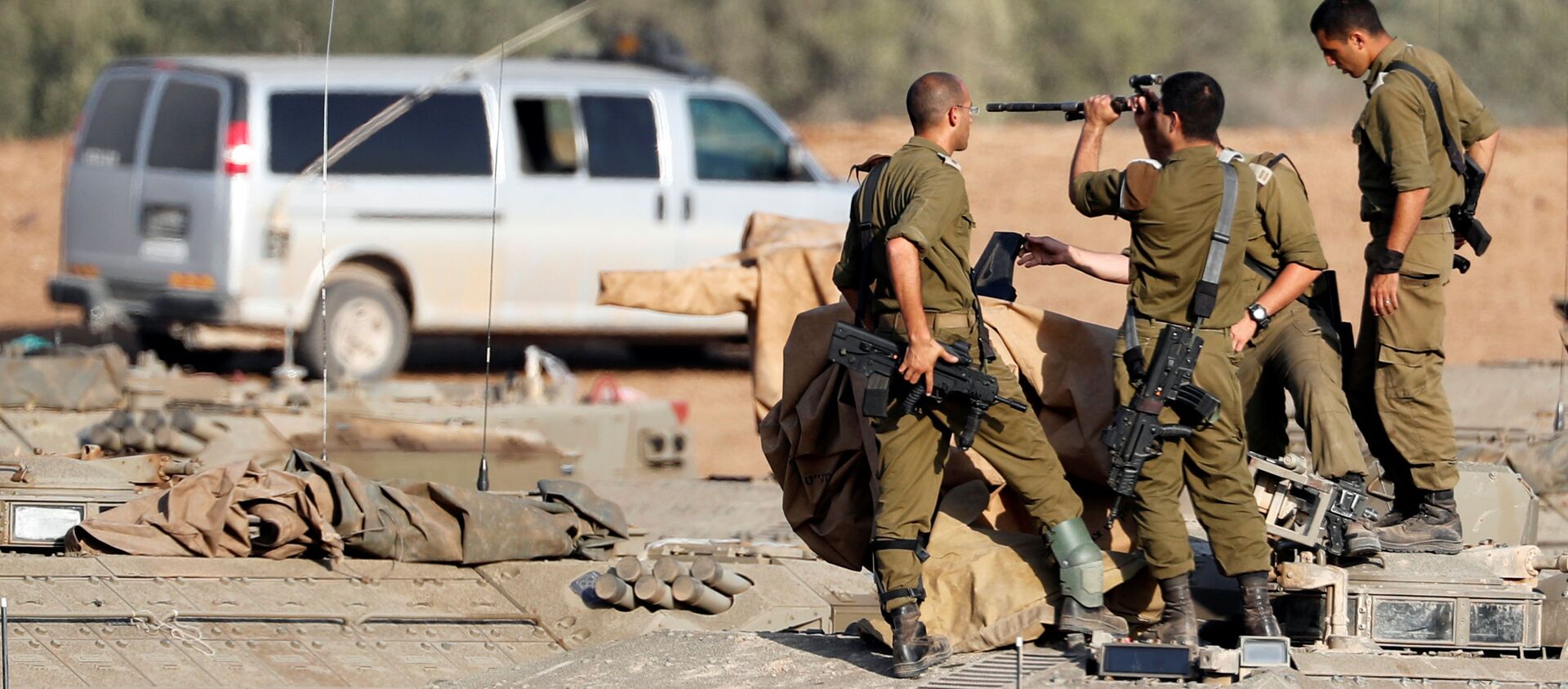 جنود إسرائيليون يفحصون سلاحهم وهم يقفون فوق ناقلة جنود مدرعة في منطقة تجمع بالقرب من الحدود مع غزة في جنوب إسرائيل - سبوتنيك عربي, 1920, 22.04.2021