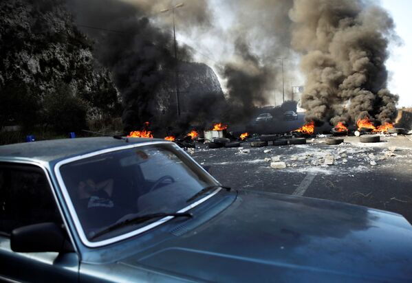 رجل ينام في سيارة بجوار إطارات محترقة على الطريق السريع خلال الاحتجاجات المستمرة المناهضة للحكومة في منطقة نهر الكلب، لبنان 13 نوفمبر 2019 - سبوتنيك عربي