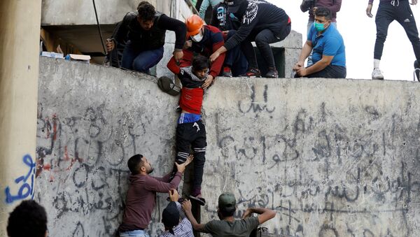 المتظاهرون يساعدون شابًا مصابًا بعد إصابته بحجر أثناء الاحتجاجات المستمرة المناهضة للحكومة في بغداد - سبوتنيك عربي
