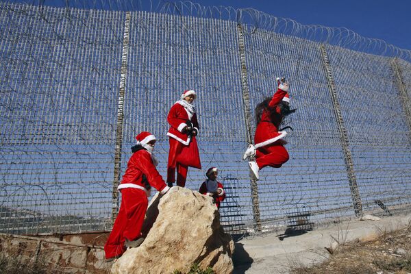 فلسطينيون يرتدون زي بابا نويل عند حاجز بالقرب من مدينة بيت لحم، الضفة الغربية 23 ديسمبر 2019 - سبوتنيك عربي