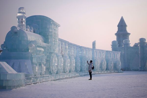 رجل يقف أمام منحوتة جليدية على شكل قطار، في إطار مهرجان هاربن الدولي السنوي للمنحوتات الثلجية في مدينة هاربن، الصين 5 يناير 2020 - سبوتنيك عربي
