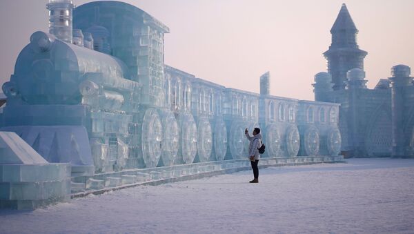 رجل يقف أمام منحوتة جليدية على شكل قطار، في إطار مهرجان هاربن الدولي السنوي للمنحوتات الثلجية في مدينة هاربن، الصين 5 يناير 2020 - سبوتنيك عربي