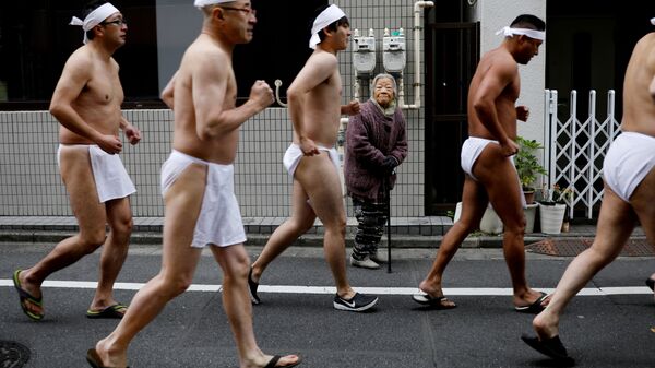 امرأة تنظر إلى رجال يبانيون يركضون حول معبد تيبوزو إنراي، استعدادا للسباحة في المياه الجليدية في إطار مراسم تطهير الروح وتمنياتهم بصحة جيدة في العام الجديد في طوكيو، اليابان 12 يناير 2020 - سبوتنيك عربي