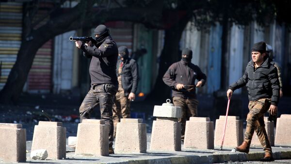 أحد أفراد قوات الأمن العراقية يطلق الغاز المسيل للدموع على المتظاهرين خلال الاحتجاجات المستمرة المناهضة للحكومة في بغداد - سبوتنيك عربي