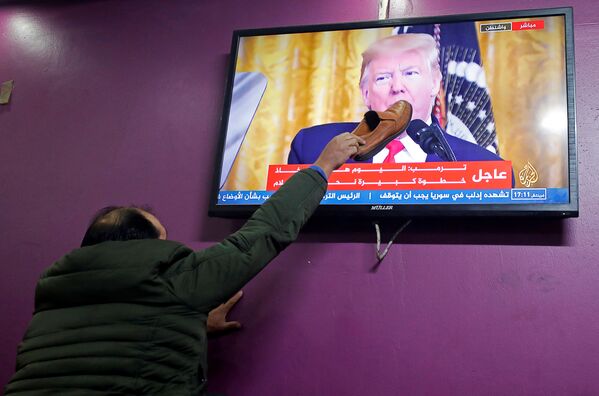 فلسطيني يضع حذاءًا على شاشة تلفزيون في مقهى في الخليل، خلال إعلان الرئيس الأمريكي دونالد ترامب لـصفقة القرن، الضفة الغربية 28 يناير 2020 - سبوتنيك عربي